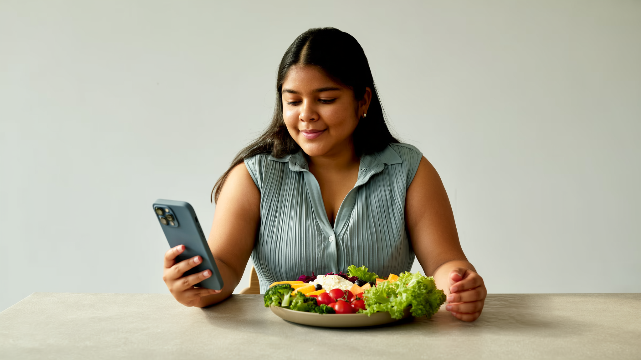 Mujer joven mirando su teléfono con un video de dieta viral mientras tiene frente a sí un plato balanceado con verduras, proteína y fruta