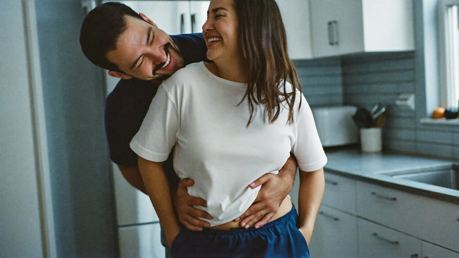 Pareja riendo abrazada en la cocina por la mañana